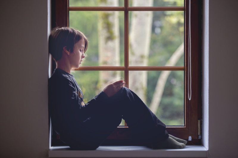 Cute school preteen child, boy, sitting on window at home, playing on mobile