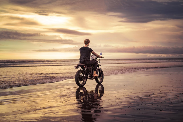 A man riding a motorcycle at the seashore in a cloudy sky 