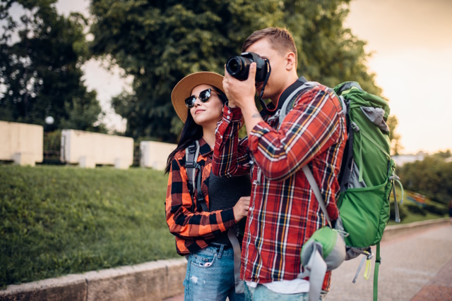 Hikers with backpacks go sightseeing in tourist town and makes photo for memory. Summer hiking. Hike adventure of young man and woman