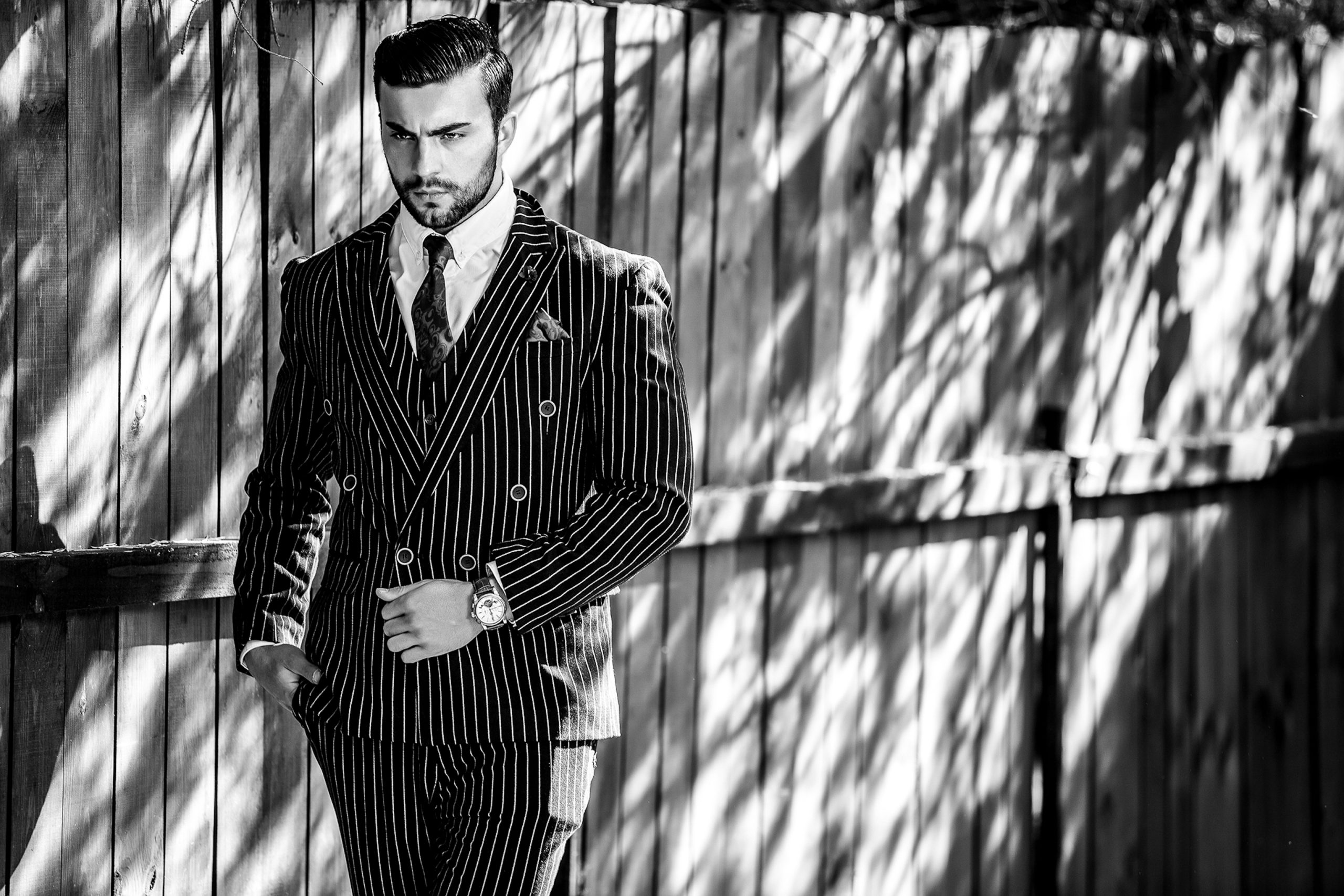 Portrait of young beautiful fashionable man against wooden fence In classic suit. Black-white outdoor fashion photo.
