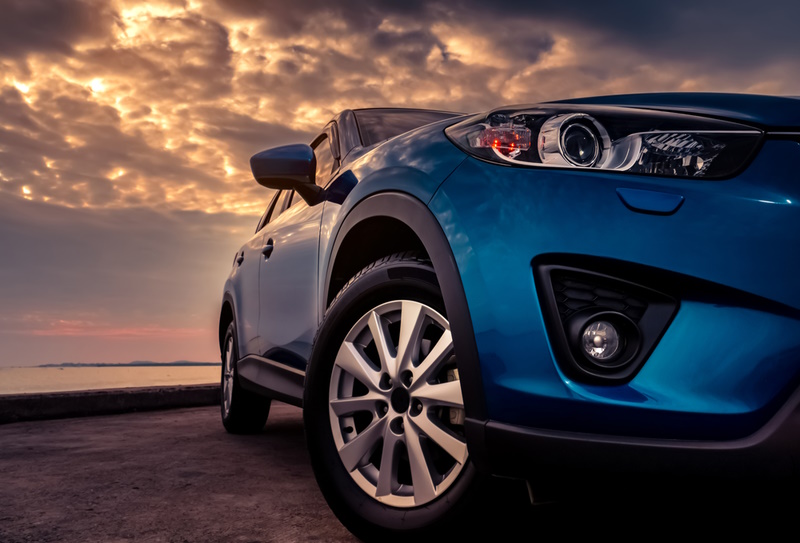 Blue SUV car with sport and modern design parked on concrete road by the sea at sunset in the evening. Hybrid and electric car technology concept. Automotive industry. Headlamp and fog lamp light.