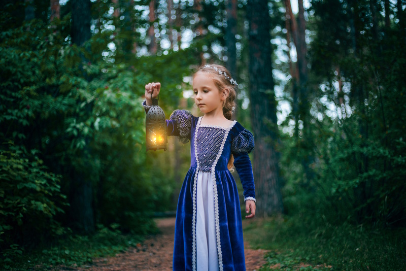 A little girl with white hair in a purple medieval dress stands with a lamp.
