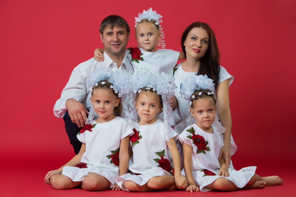 Big happy family: parents are father, mother and children are twins in embroidered dresses with an ornament on a red background in the studio.