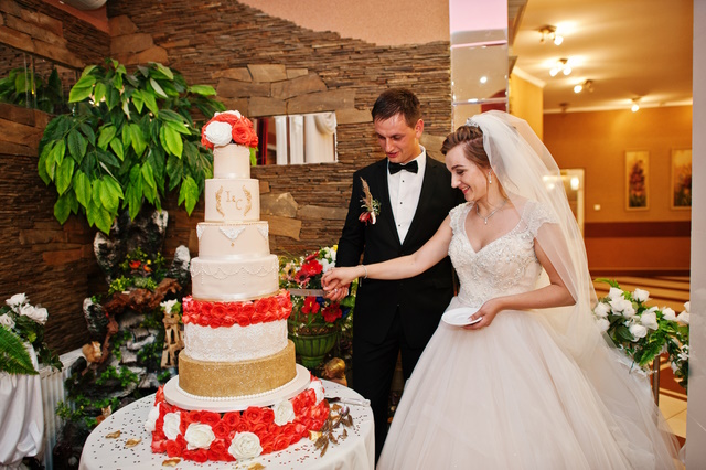 Gorgeous wedding couple cutting their cake with knife in restaurant.