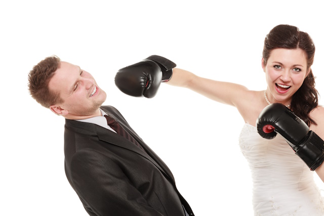 Funny Wedding Photography Ideas: Top Trends - Funny married couple fighting. Wife showing her husband who's boss. Angry woman bride in wedding dress boxing punching man groom isolated on white